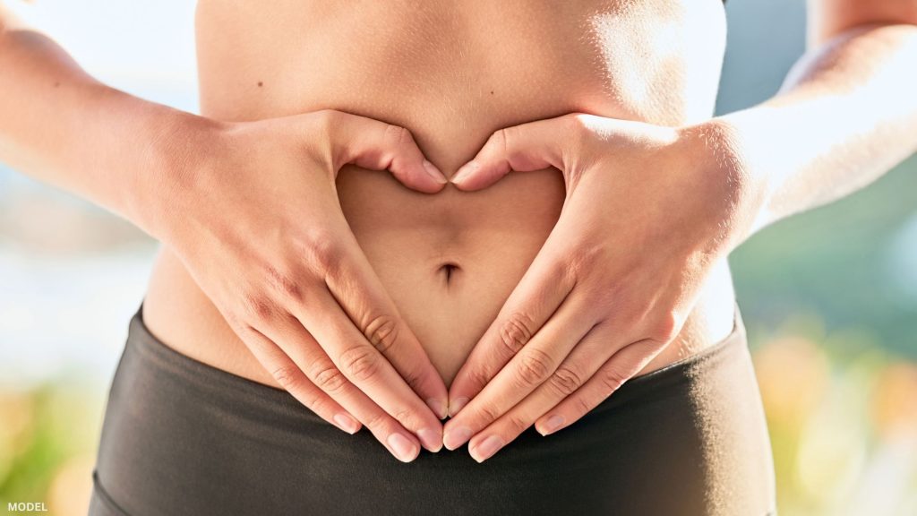 Woman standing with hands shaped like a heart around belly button (model)