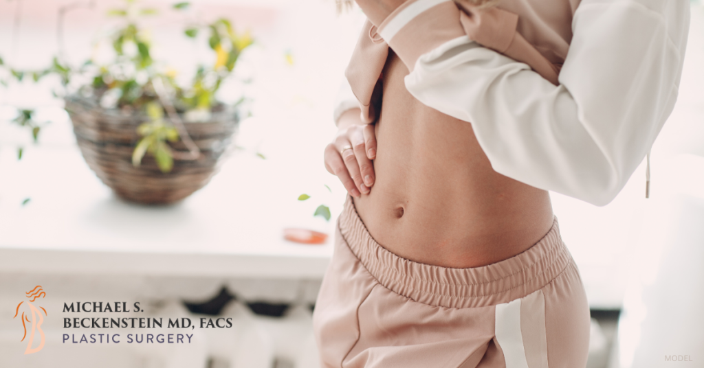 Woman (model) holding up her shirt, showing off her toned stomach.